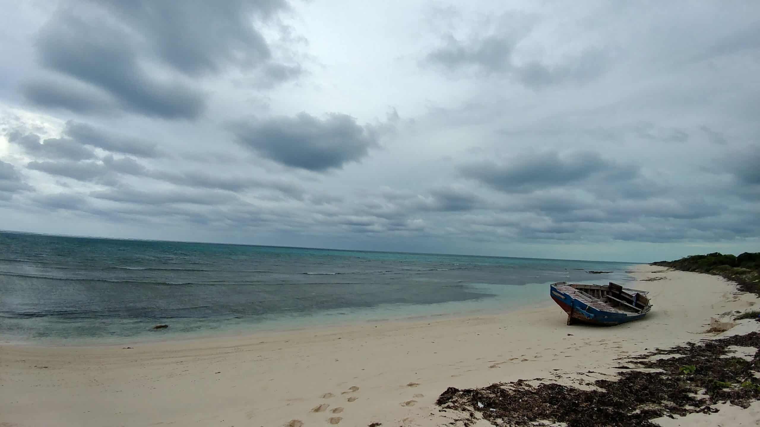 Serene beach with boat and cloudy sky in Turks & Caicos Islands.