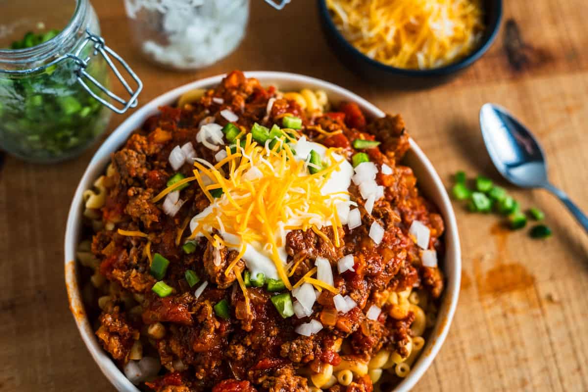 Bowl of Chili Mac topped with sour cream, onion, and jalapenos