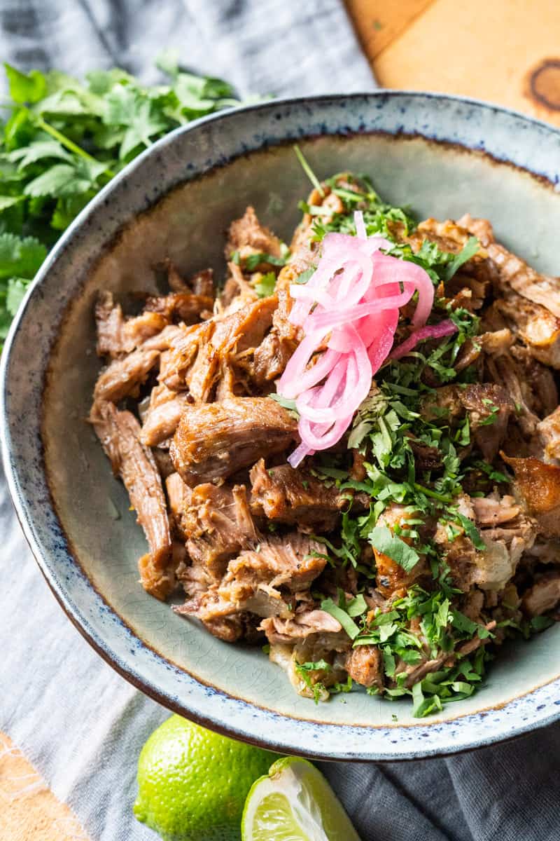 Pork Carnitas in a bowl garnished with cilantro and pickled red onion