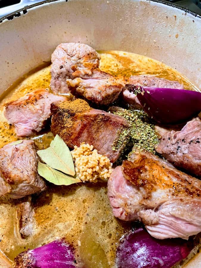 Pork shoulder seasoned with oregano, garlic, bay leaves and red onion simmering in a dutch oven