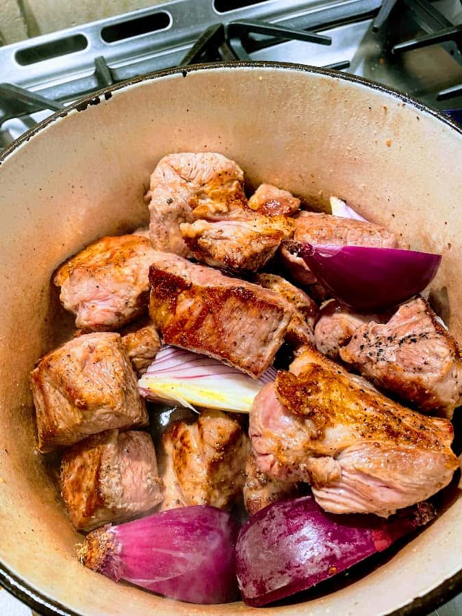 browned pork shoulder in a pot with red onions