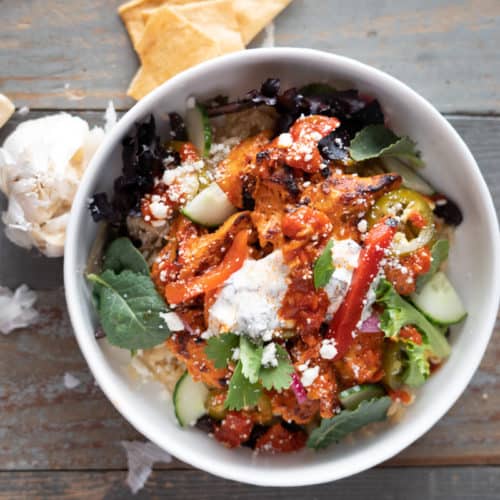 Roasted harissa chicken served over rice and salad mix with tzatziki and feta