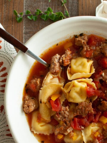 Italian sausage and tortellini soup in a white bowl with a spoon