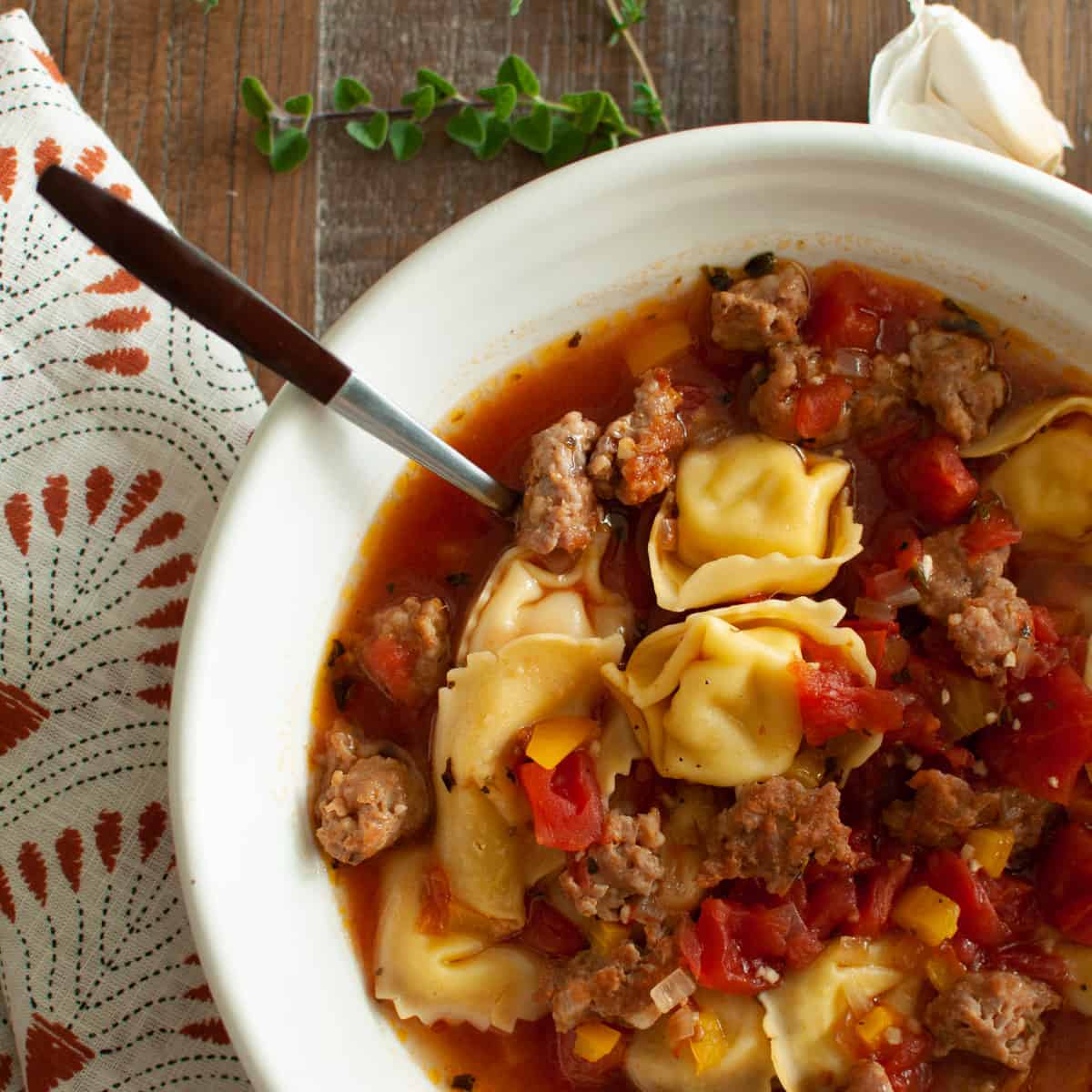 Italian sausage and tortellini soup in a white bowl with a spoon