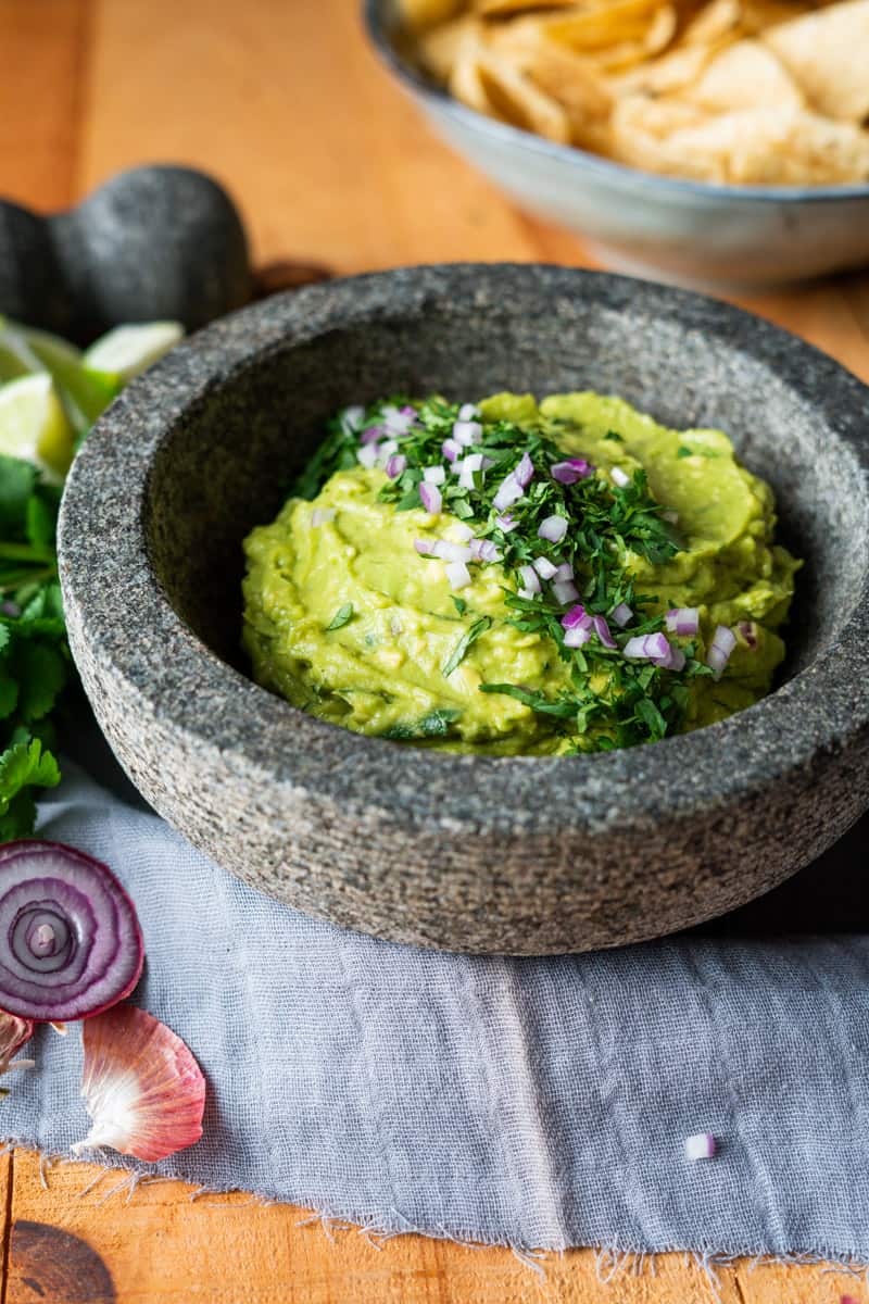 guacamole being served in a large mortar and pestle style bowl garnished with cilantro and diced red onion