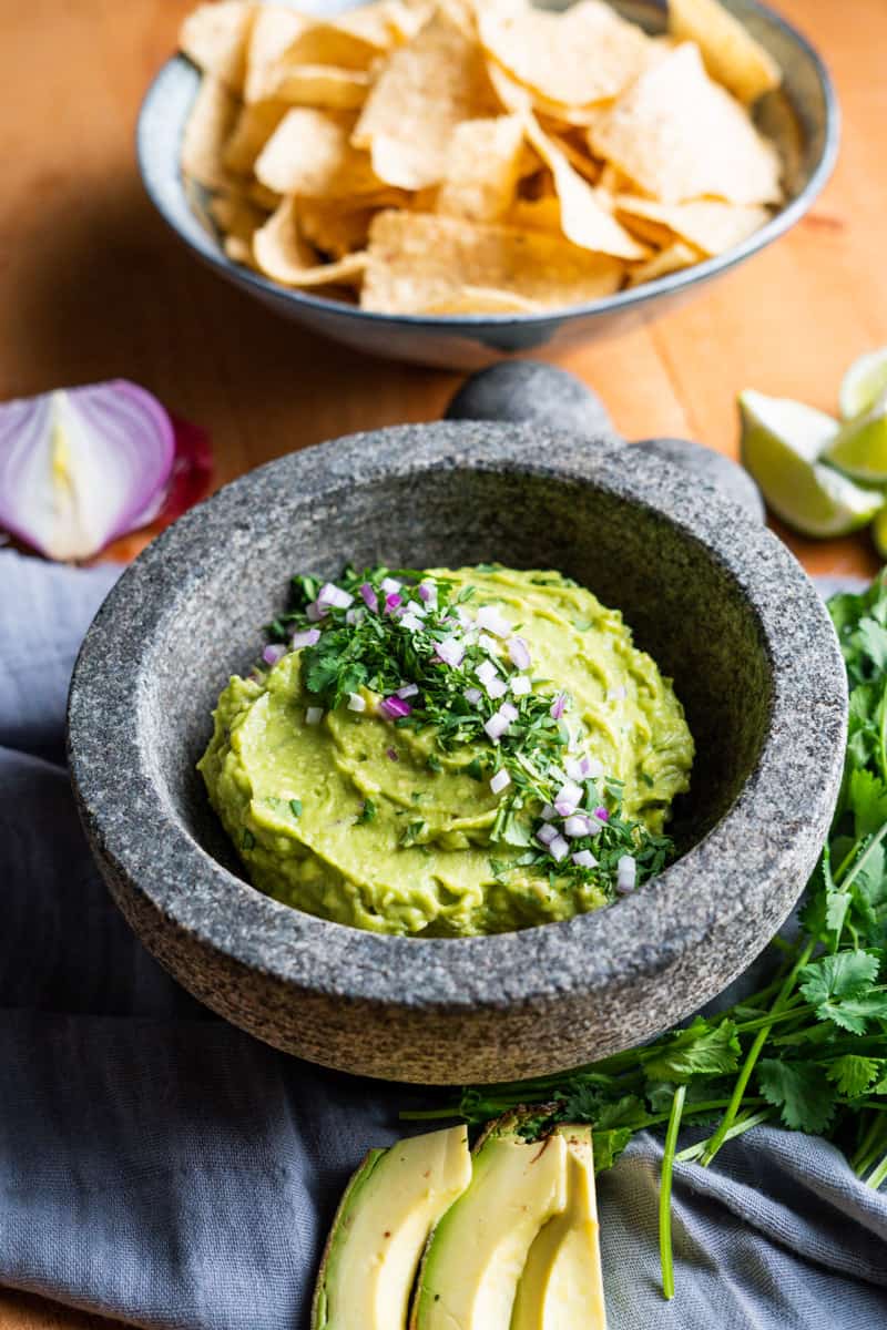 guacamole in a large mortal and pestle style bowl garnished with cilantro and diced red onion