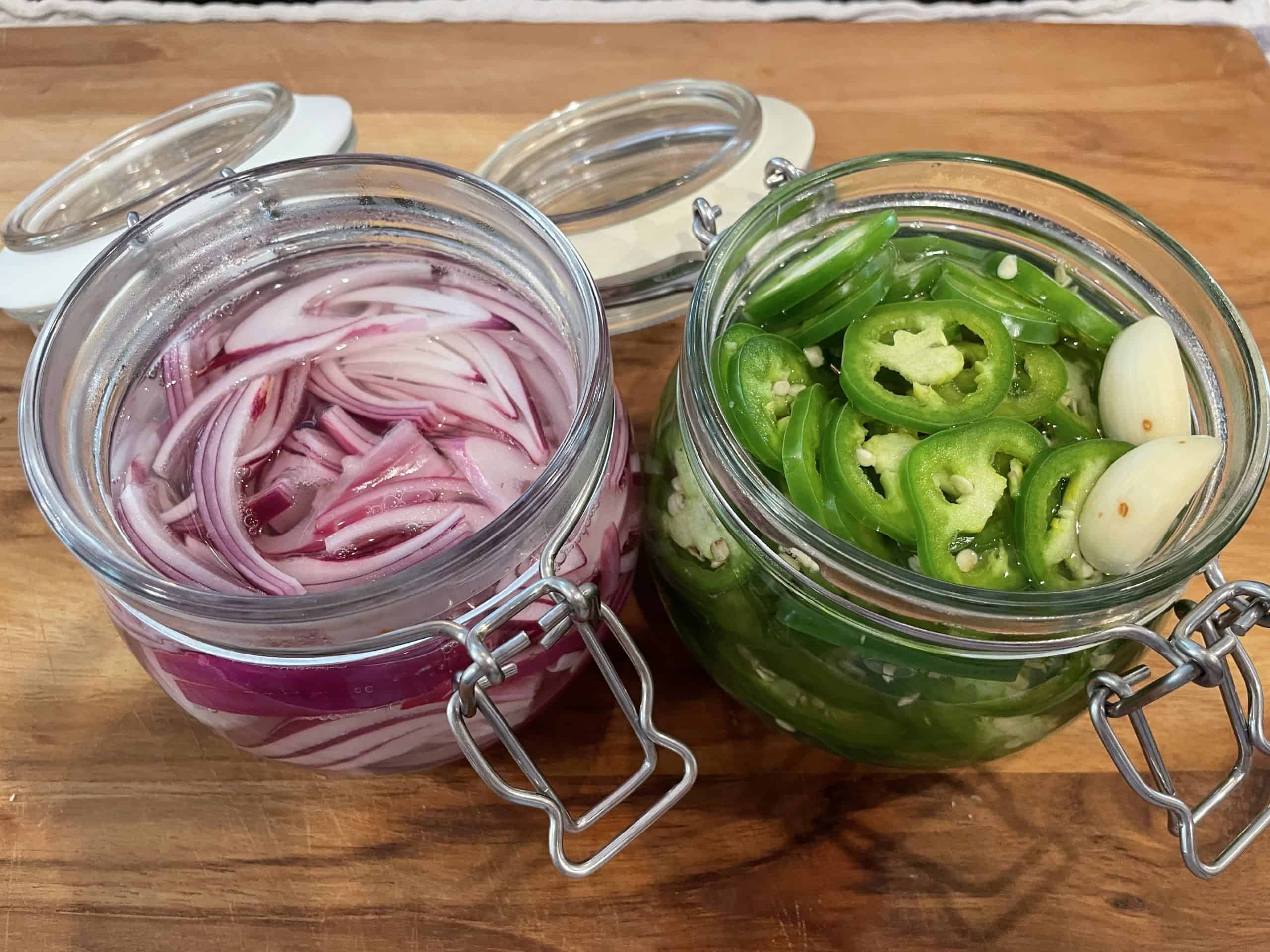 red onions and jalapenos in two separate glass jars with pickling liquid poured over