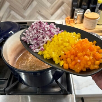 plate of diced bell peppers and onions being added to a dutch oven for chili