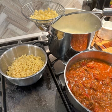 Stove top with pasta and chili in pots, scooping pasta out of boiling water