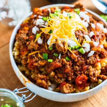 Bowl of chili Mac topped with sour cream and diced onions and jalapenos.