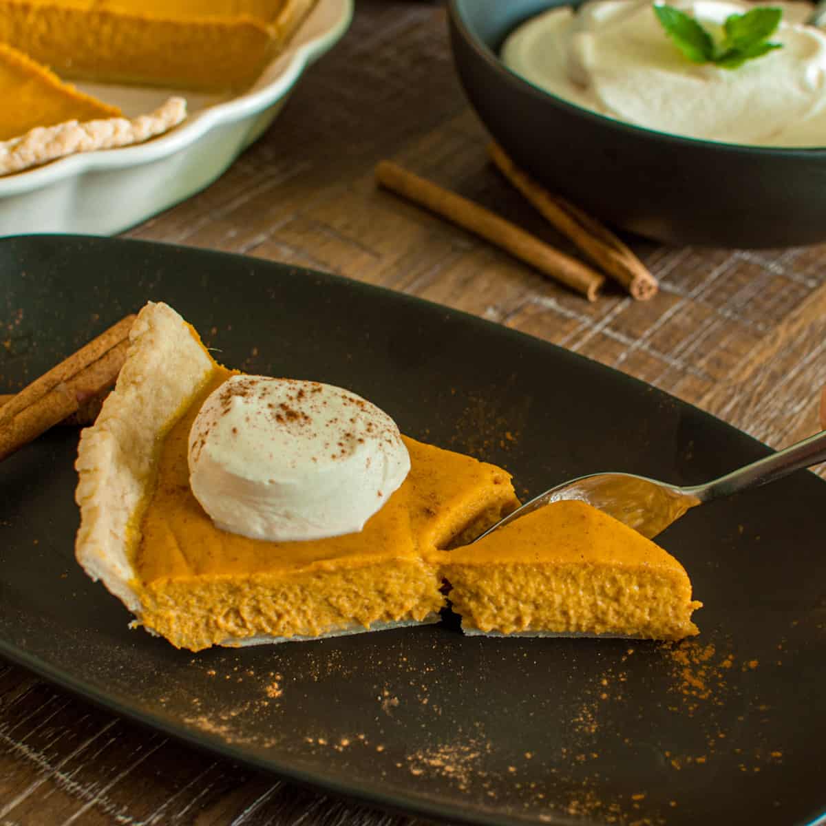 Slice of Pumpkin Pie with whipped cream and a fork cutting into it