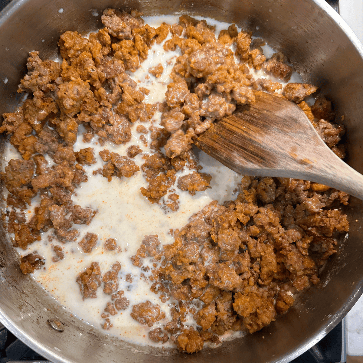 Adding milk to browned chorizo and mixing.