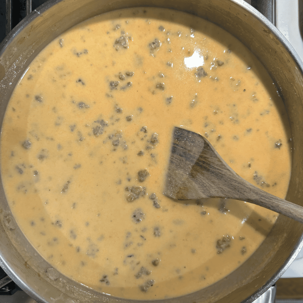 Chorizo sausage gravy simmering on the stove with a wooden spoon.