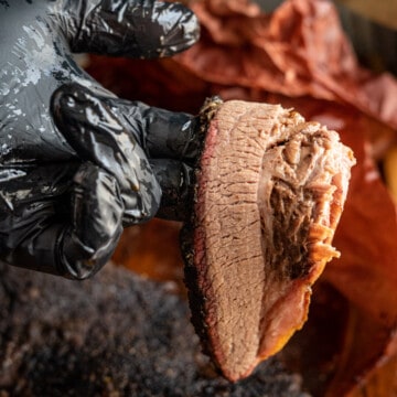 Smoked brisket, sliced, held by a black gloved hand.
