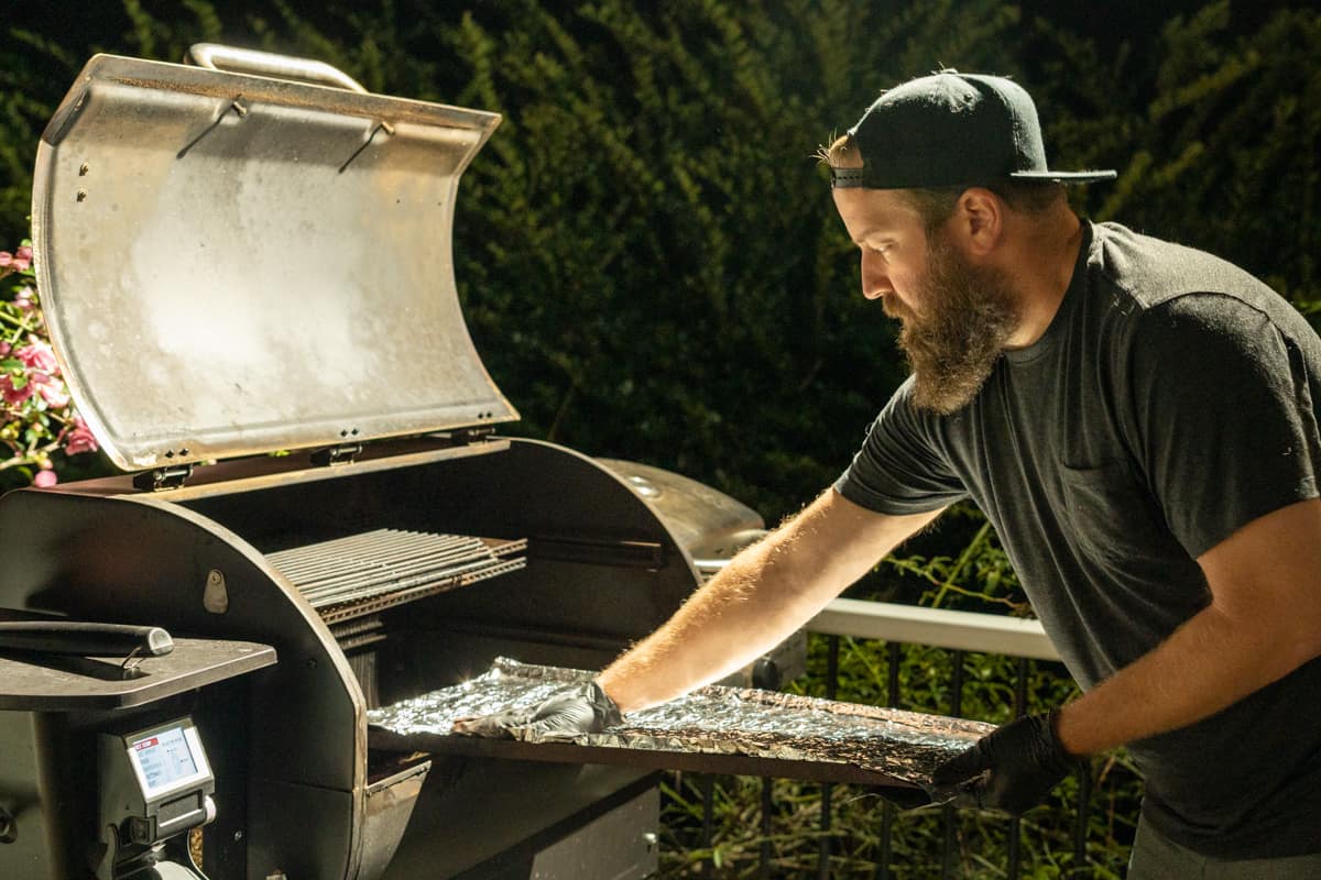 man replacing foil on the bottom of a pellet smoker