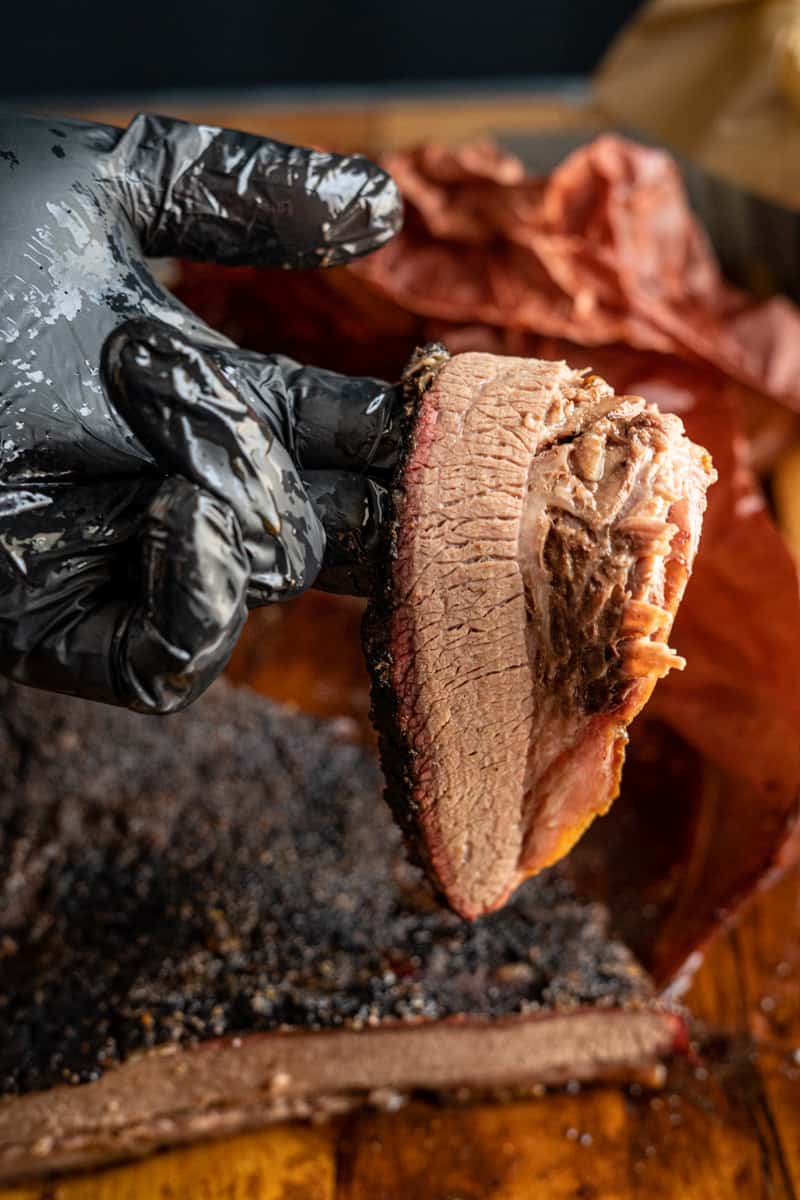 sliced brisket being held by a hand in a black glove