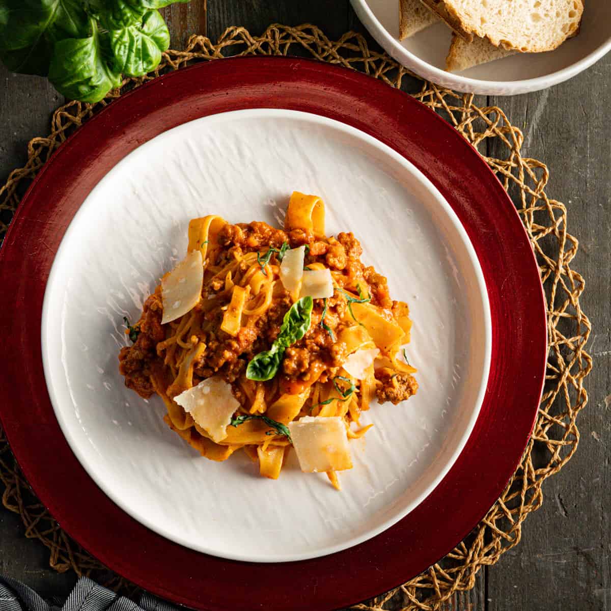 Pasta Bolognese on a white plate with a red charger