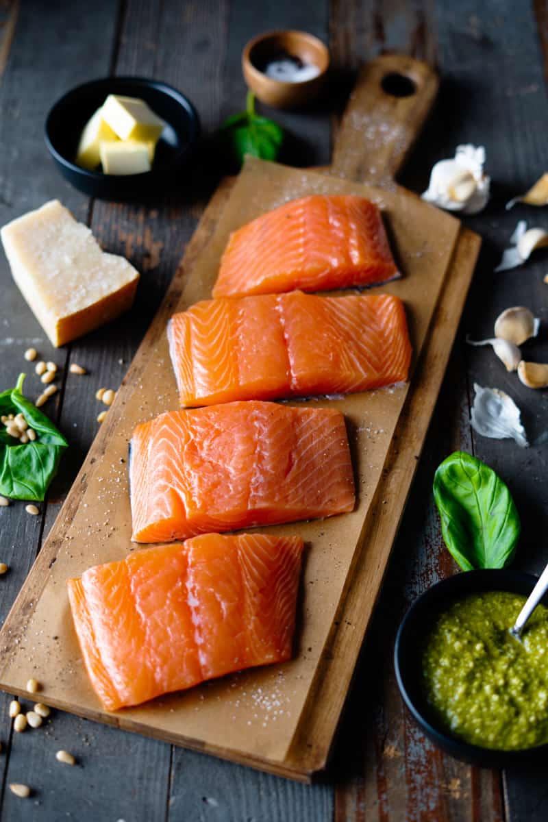 raw salmon on parchment paper next to a bowl of pesto