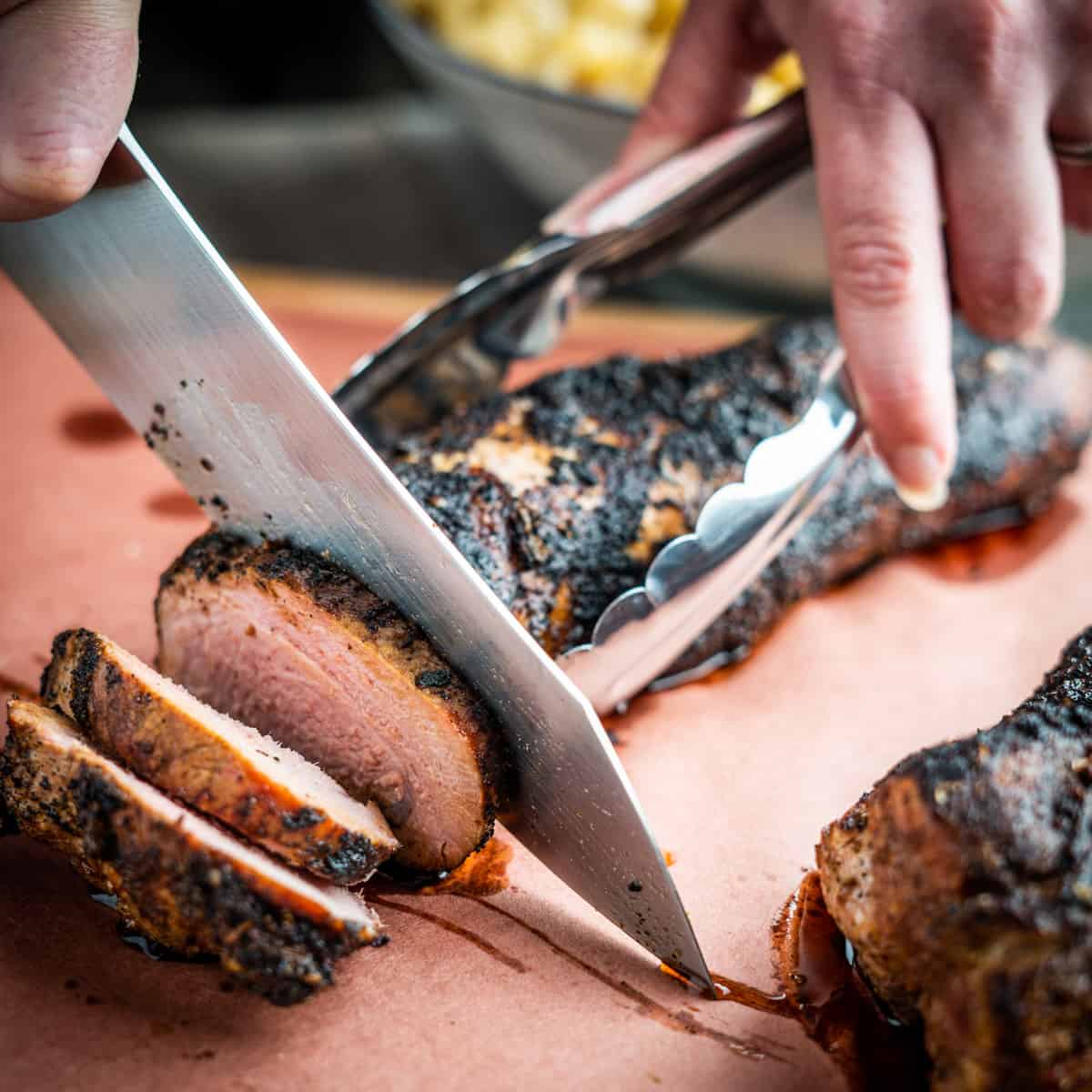 Person slicing smoked pork tenderloin with a sharp knife.