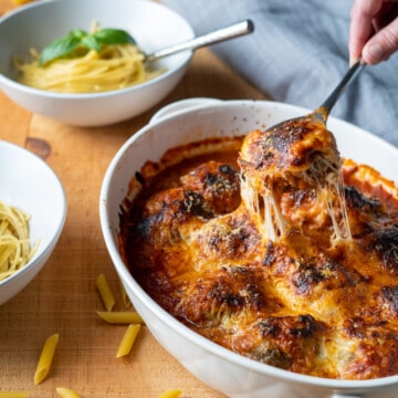 Cheese covered meatball being scooped from a dish