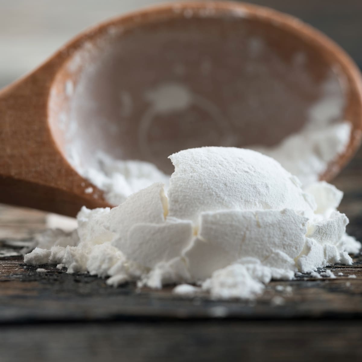 spoonful of cornstarch on a wooden table with spoon in the background