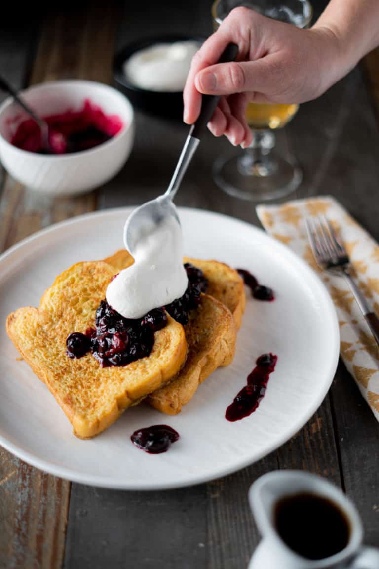 Brioche French toast being topped with berries and whipped cream