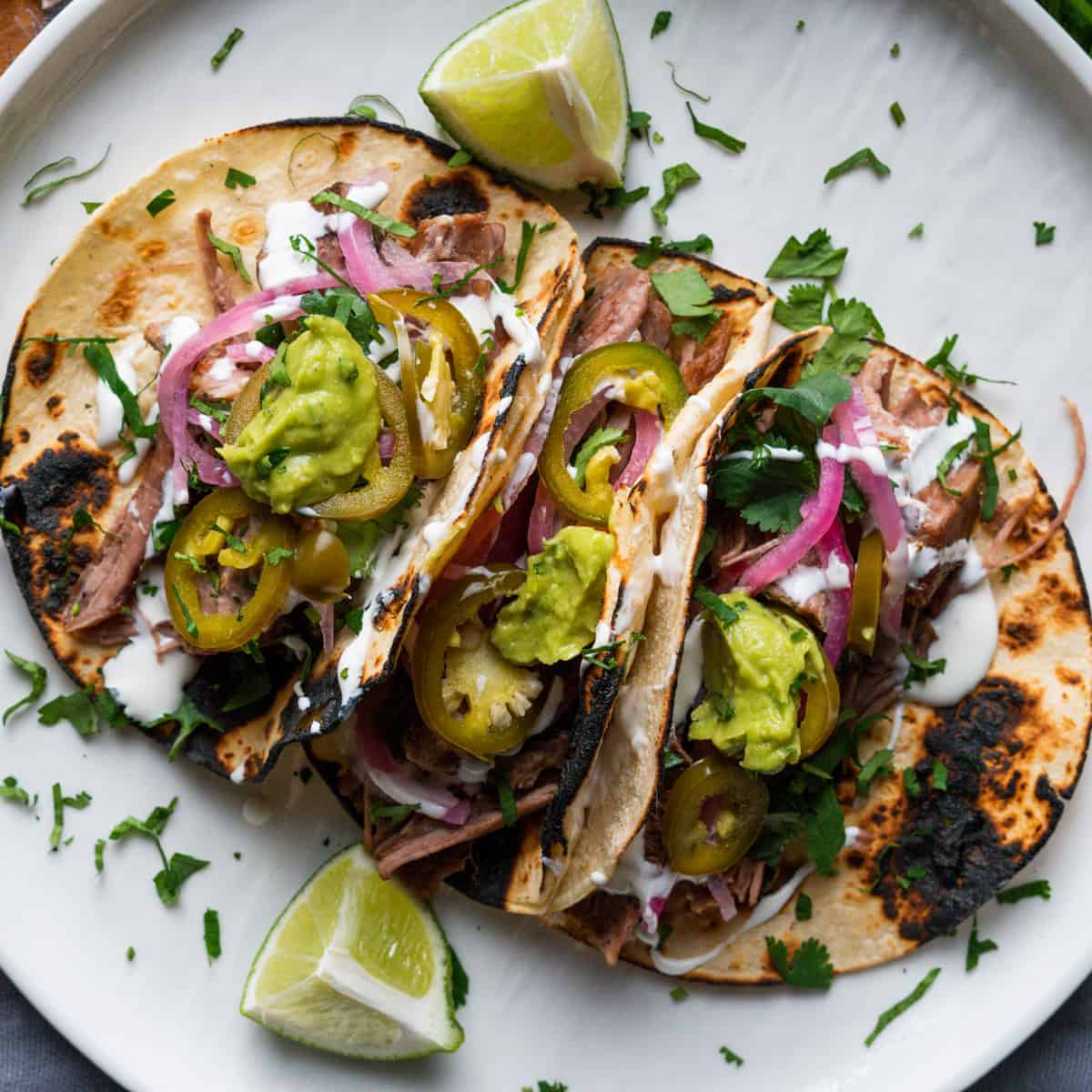 Carnitas street tacos on a white plate garnished with lime and cilantro