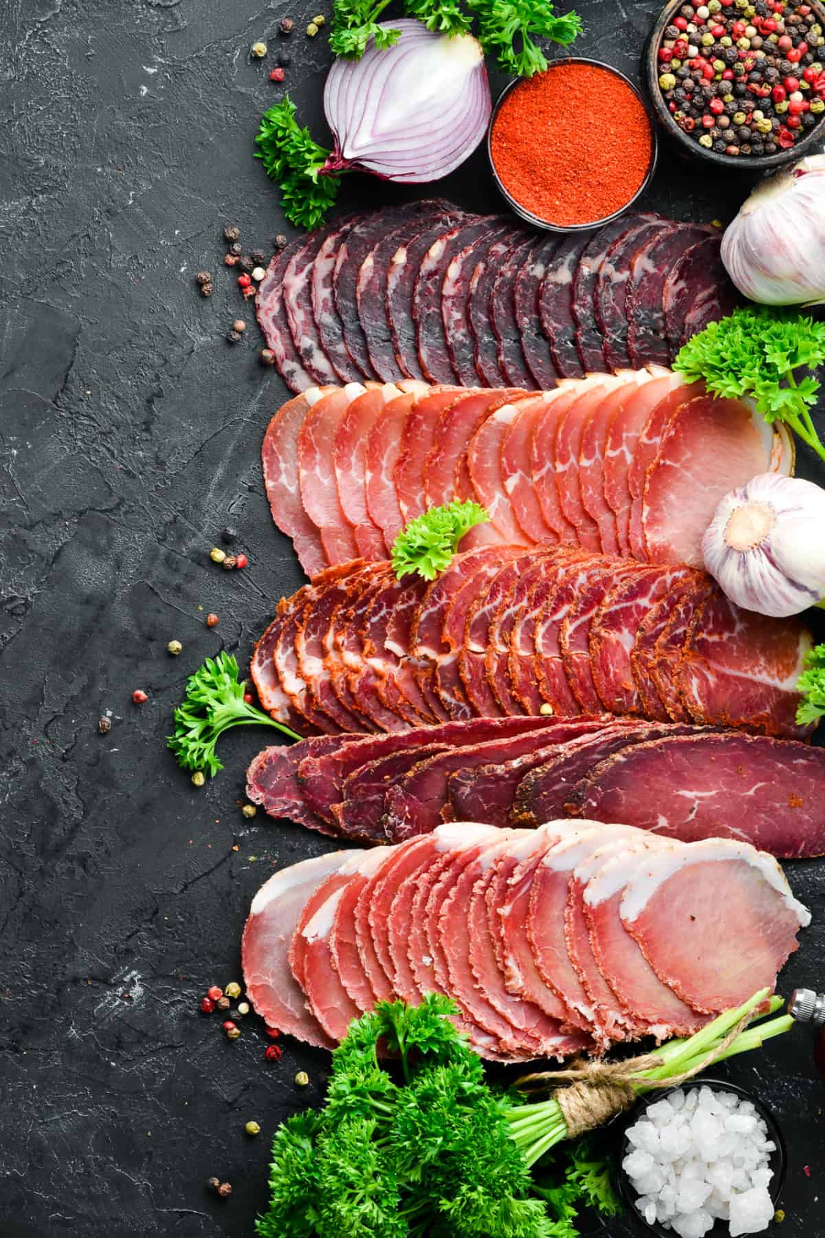 Variety of meats sliced and laid out on black slate