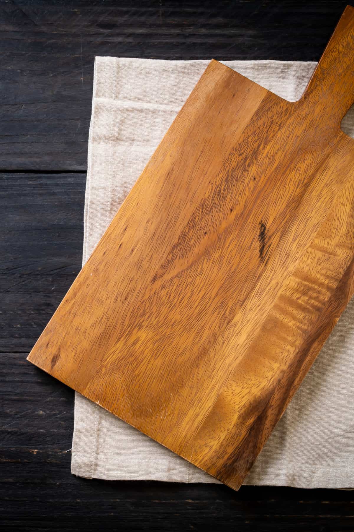 Wooden charcuterie board on a linen napkin on a dark wood table