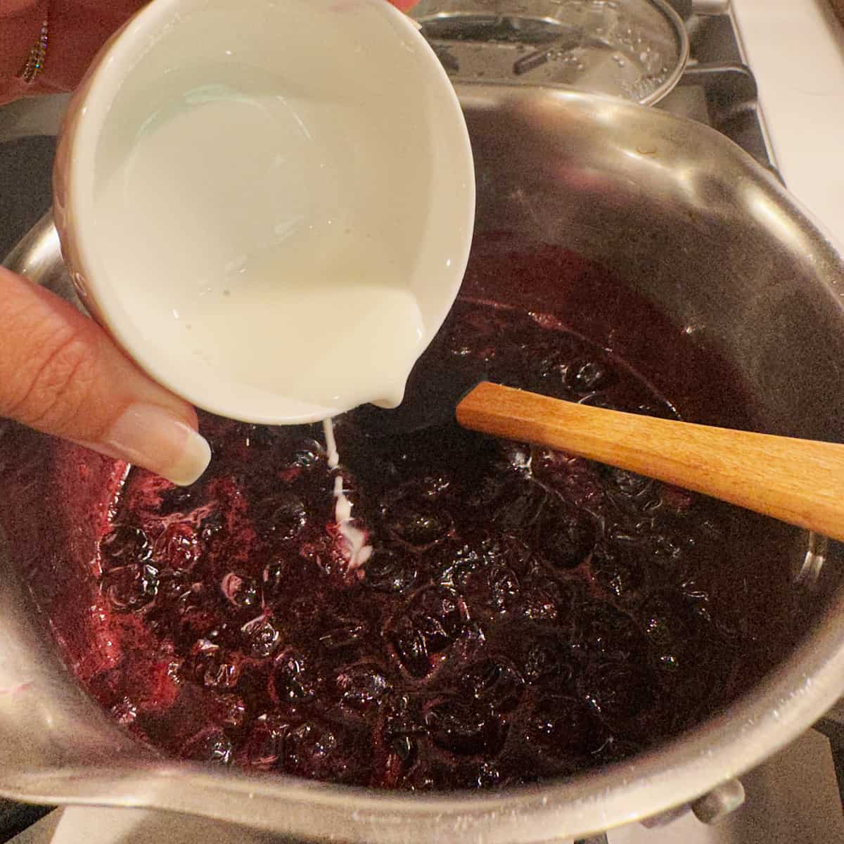 Mixing a cornstarch slurry into a blueberry sauce