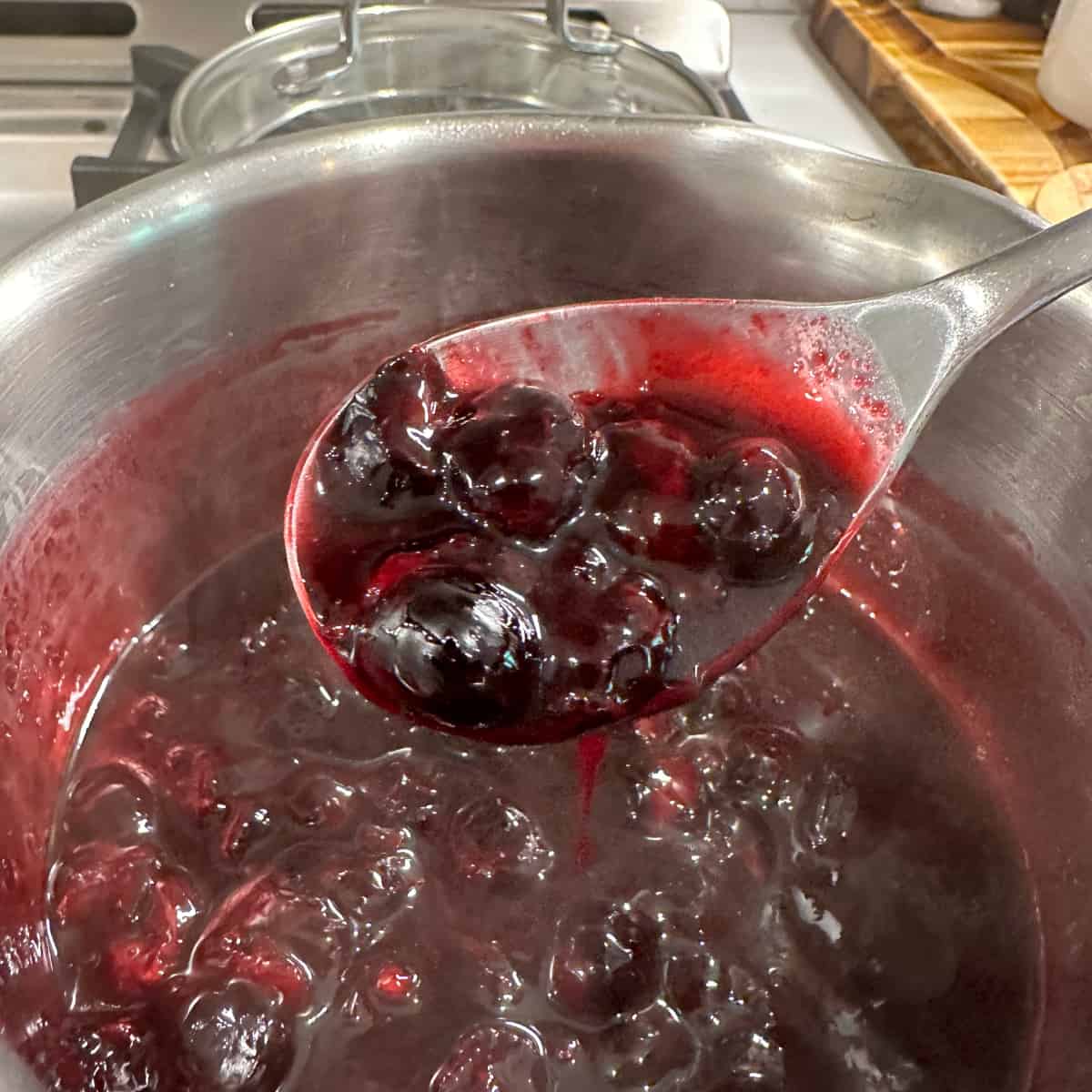 Blueberry compote on a metal spoon being scooped from a pot 