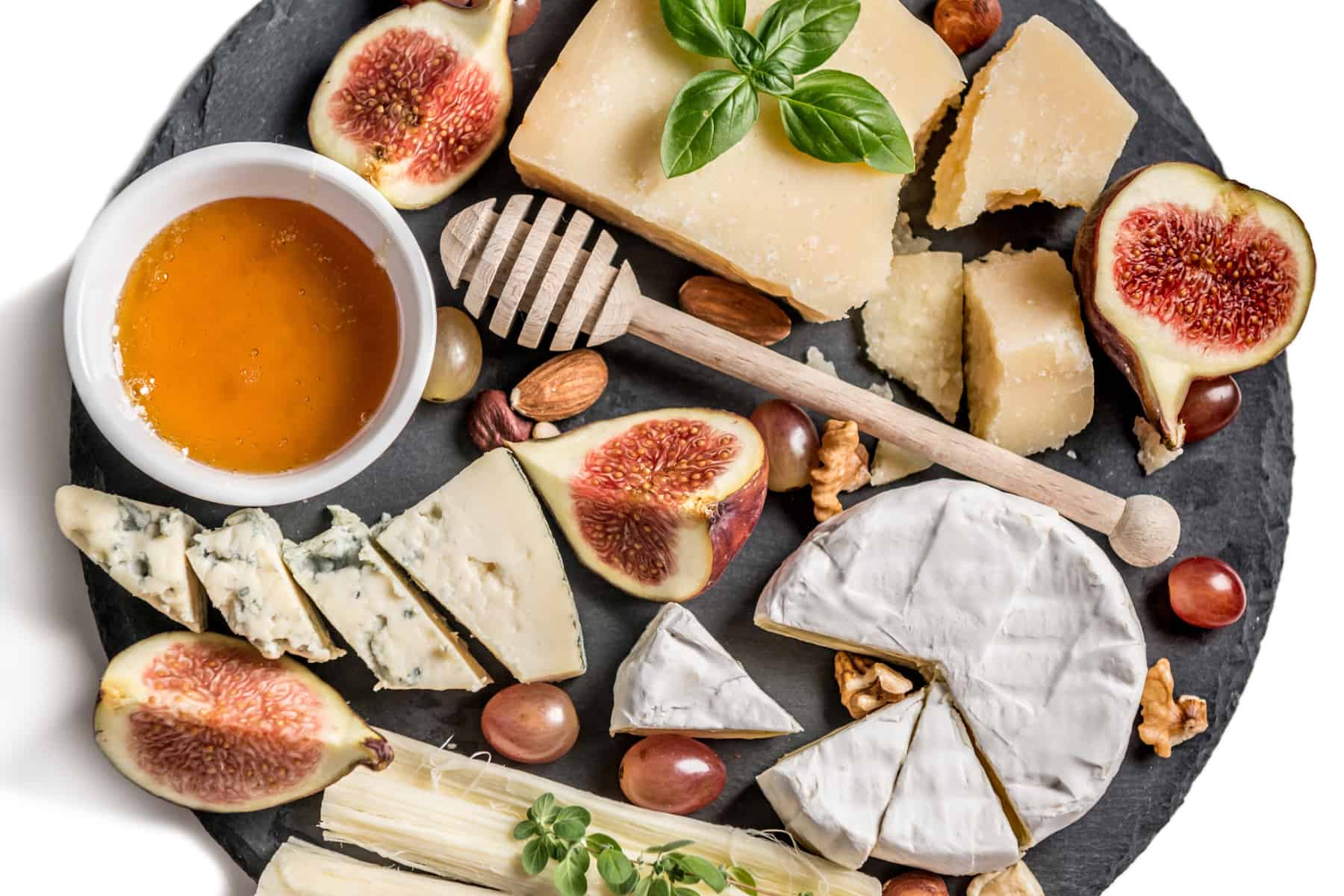 a variety of cheeses, honey, and fruit on a slate charcuterie board