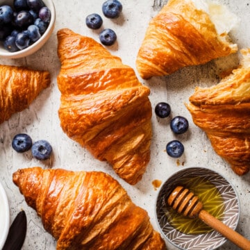 Golden croissants with fresh blueberries and honey on a rustic surface.