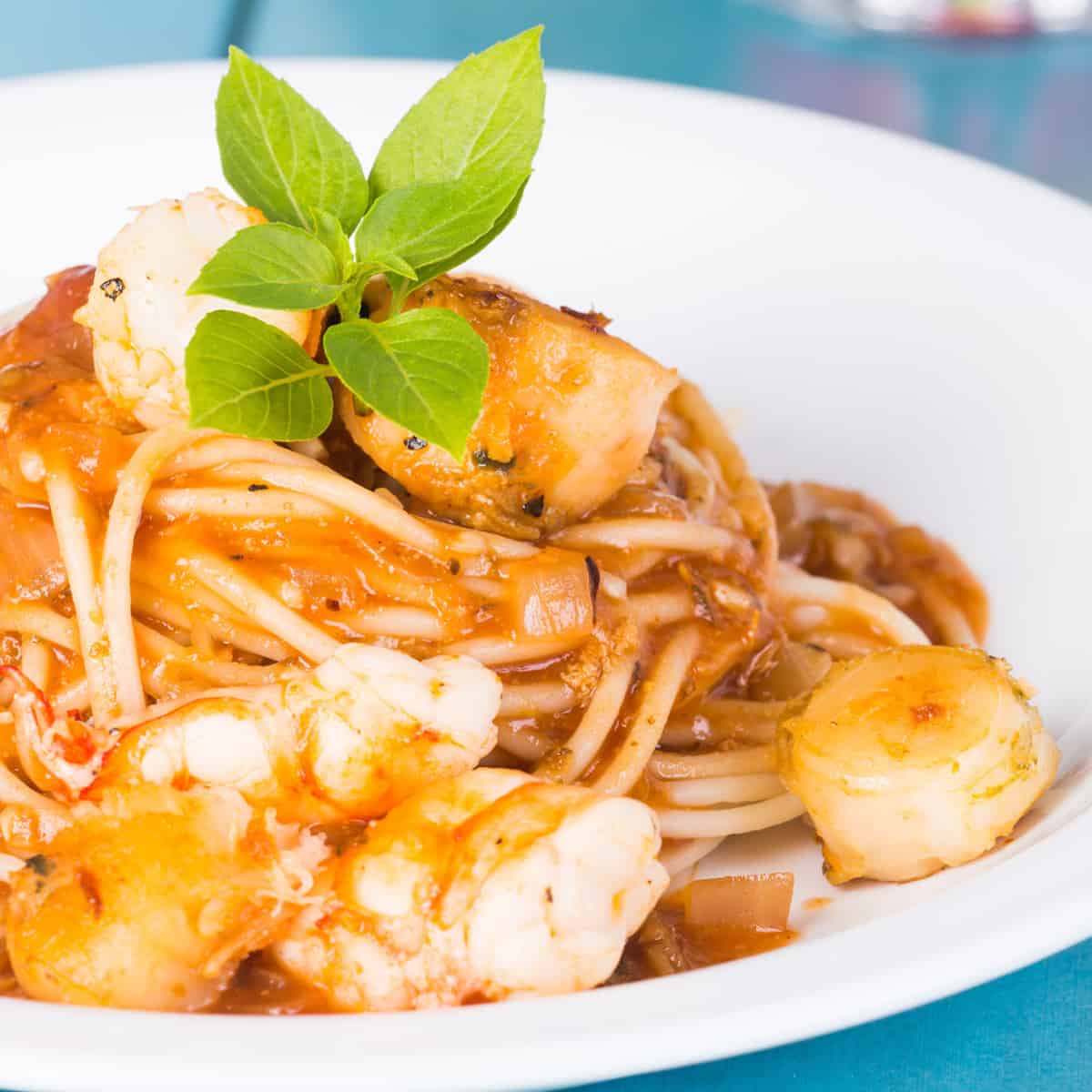 Shrimp and scallops over pasta in a light red sauce garnished with basil 