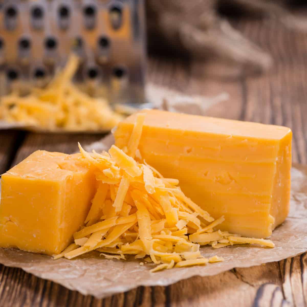 block of cheddar cheese, with some grated in the foreground