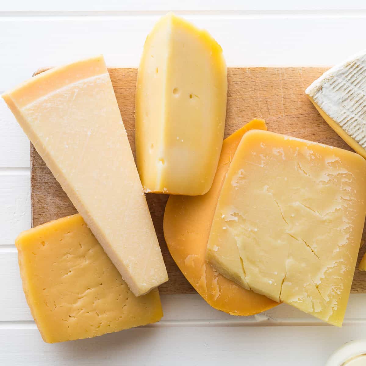 Cheddar and Gouda cheese in small wedges on a cutting board