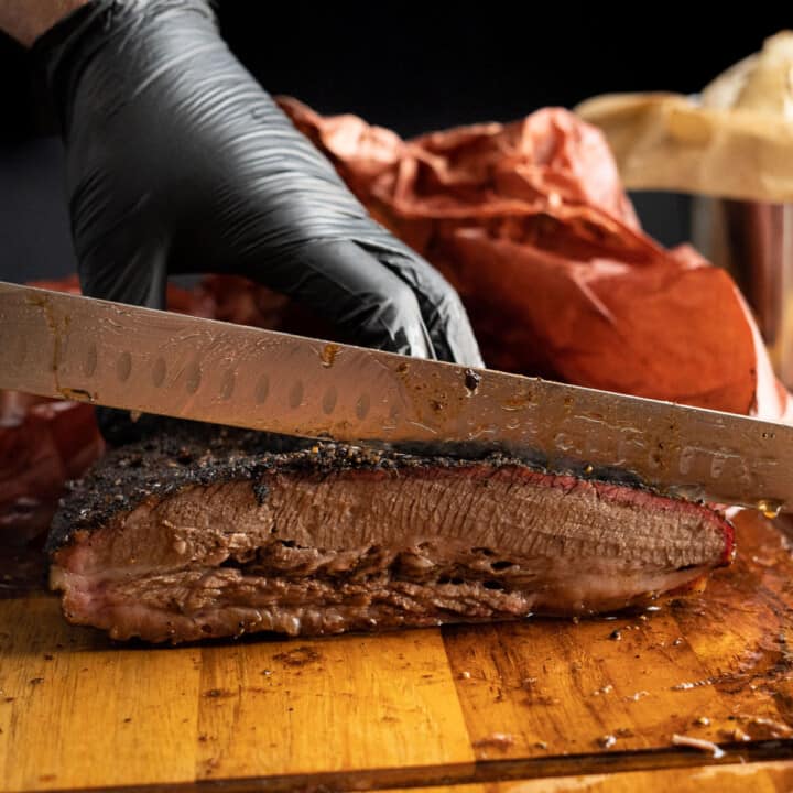 Gloved hands slicing a smoked brisket on a cutting board — gloves are one of the best pellet smoker gifts