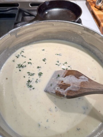 Stiring fresh thyme into a cream sauce with wooden spoon