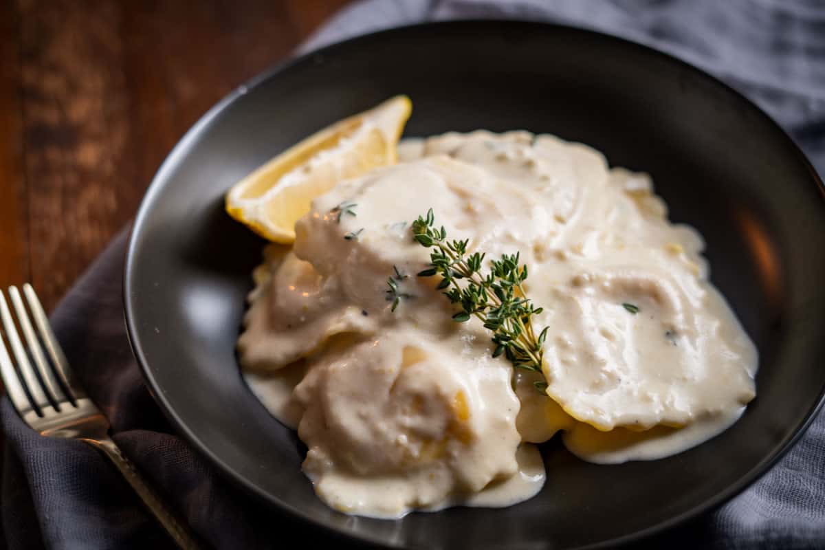 Lobster Ravioli in a cream sauce garnished with fresh thyme in a black bowl