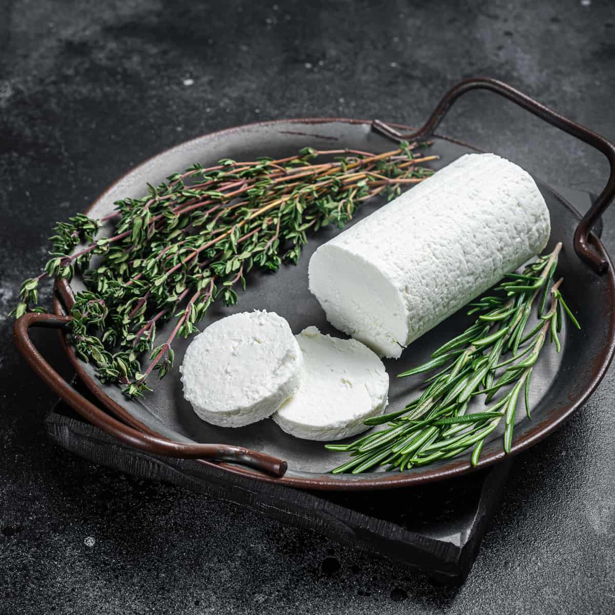 a log of goat cheese on a metal serving plate with fresh thyme and rosemary