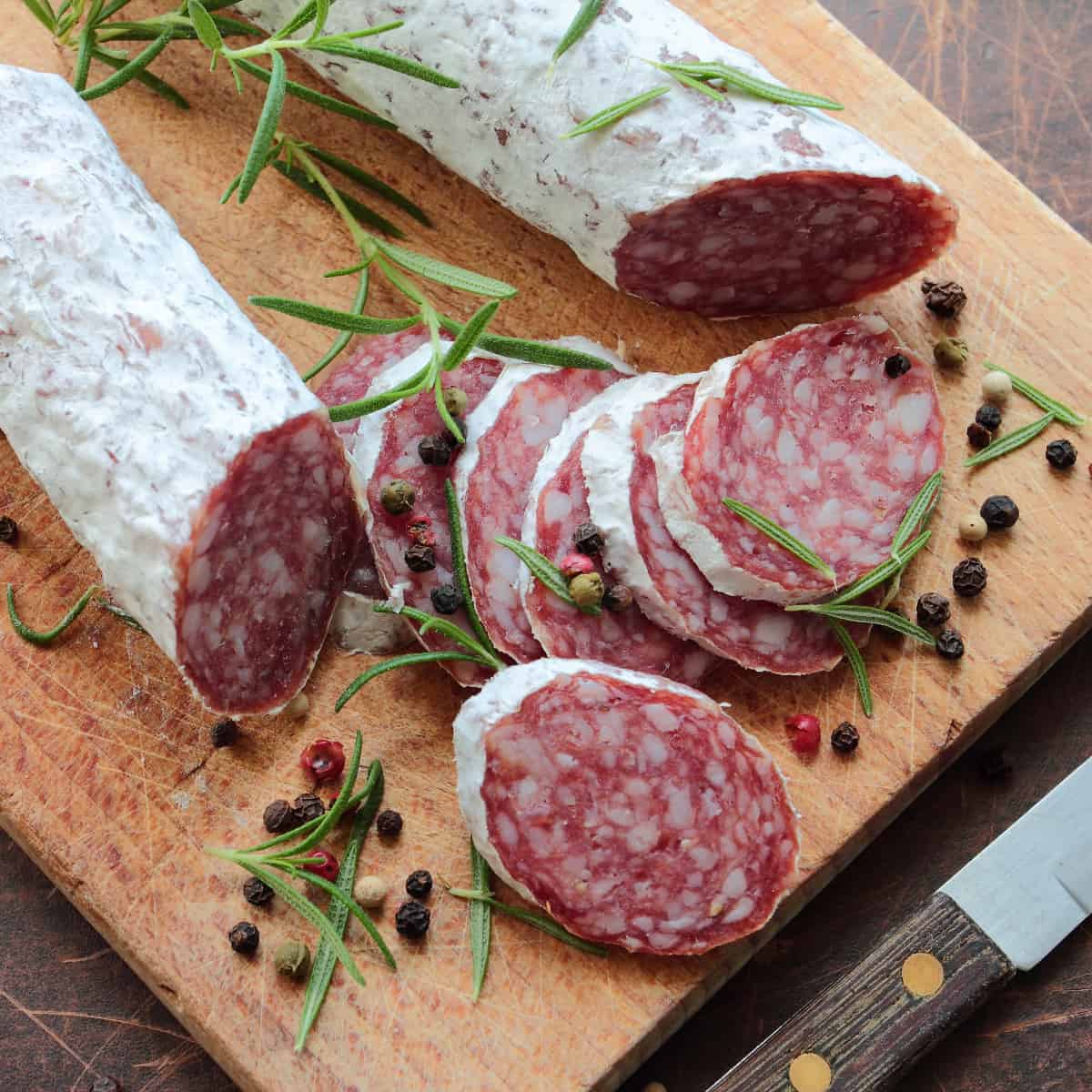 Soppressata slices on a cutting board with peppercorn and fresh herbs