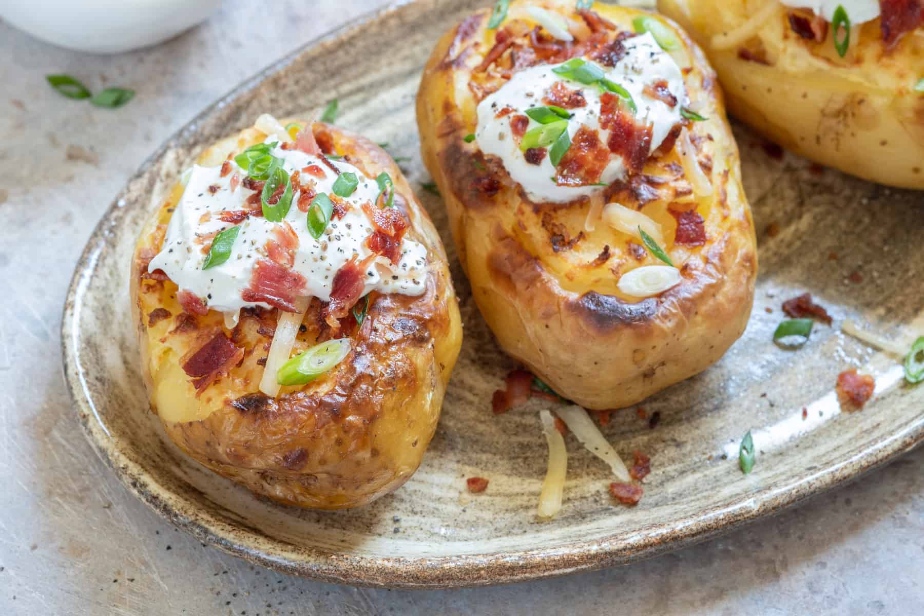 loaded baked potato with sour cream, bacon bits, and green onions on top 