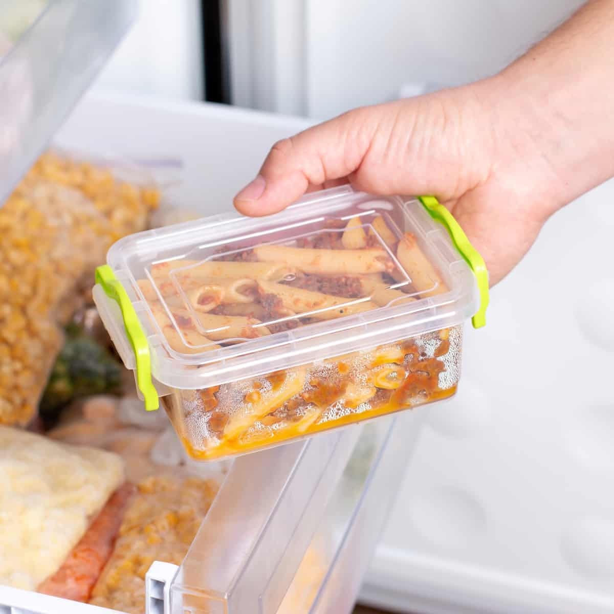 hand placing a Tupperware container of pasta into the freezer