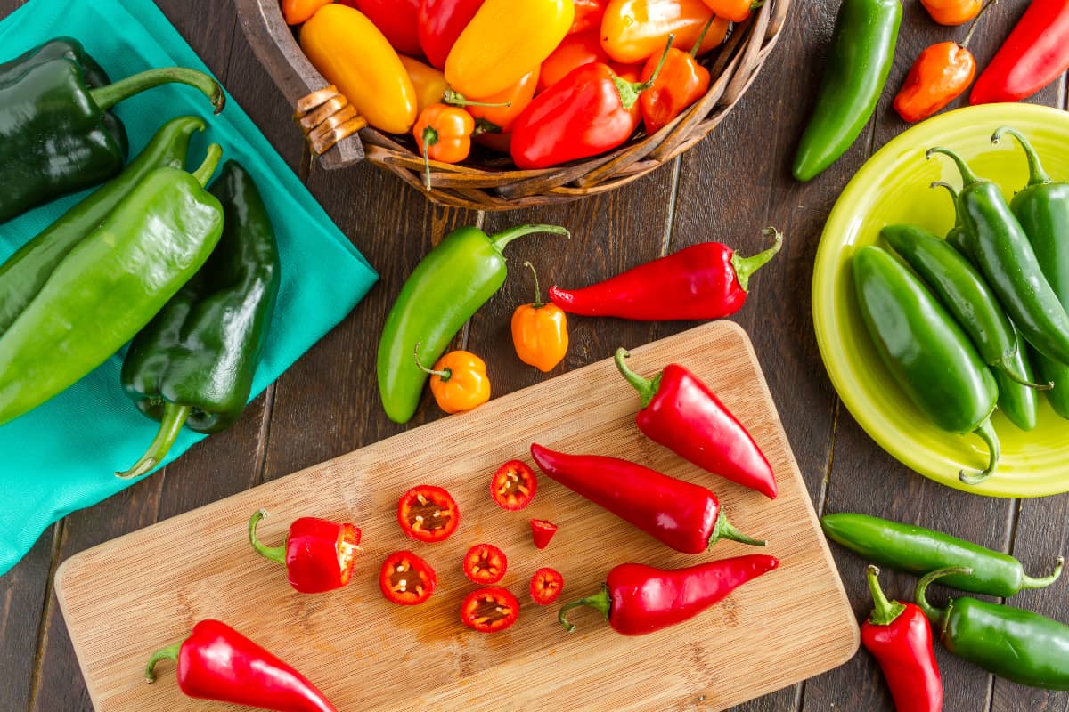 multiple types of peppers on a tabletop, cutting borad, and bowl 