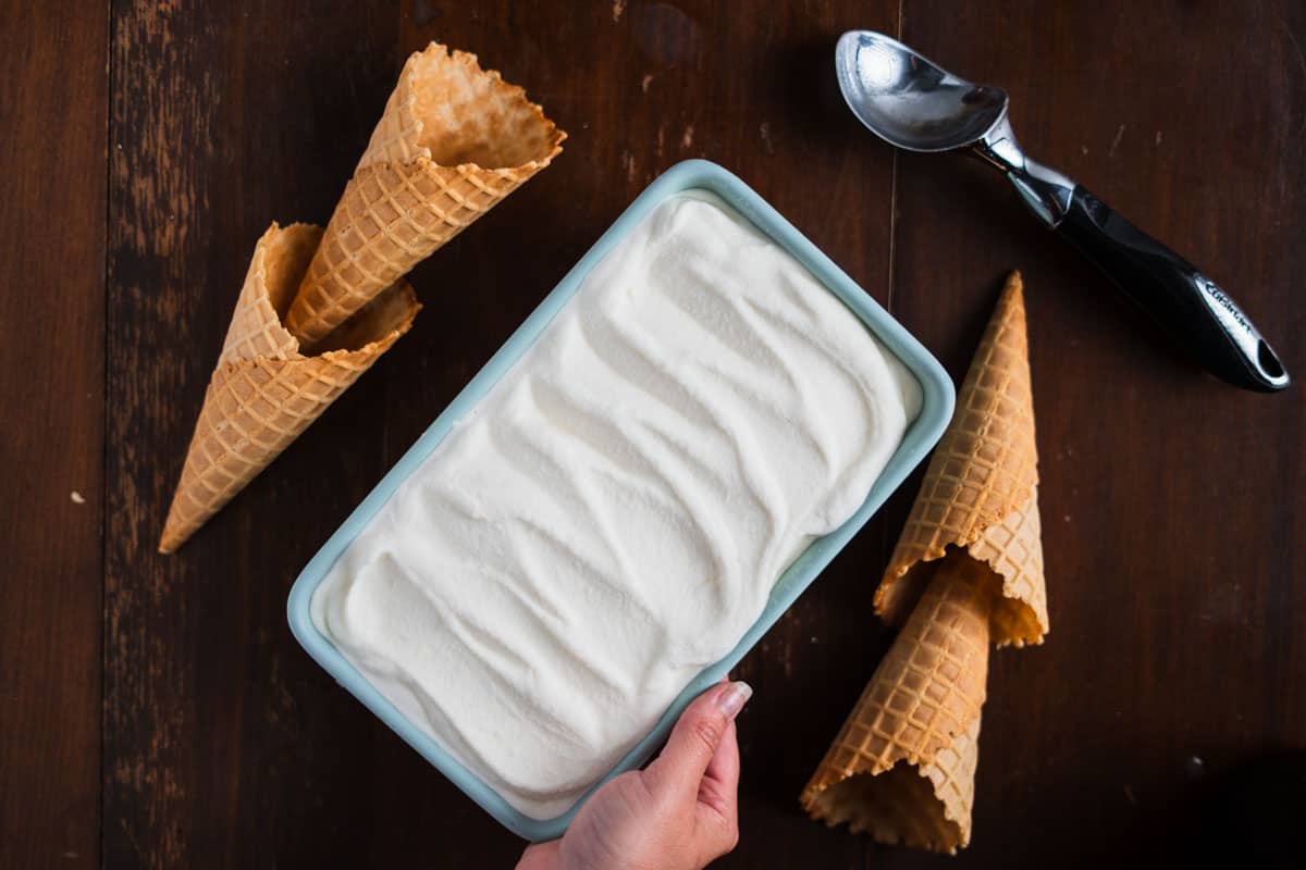 A teal loaf pan filled with ice cream next to waffle cones