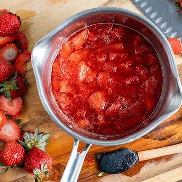 Overhead view of fresh strawberry compote in a saucepan with sliced strawberries beside it.