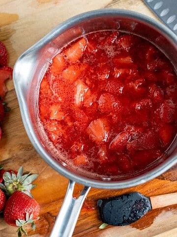 Overhead view of fresh strawberry compote in a saucepan with sliced strawberries beside it.